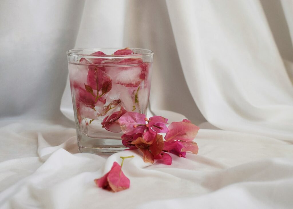 a glass filled with pink flowers on top of a white cloth